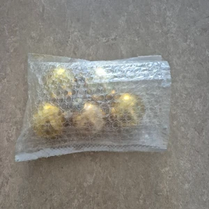 Julkulor - Fyra guldfärgade julgranskulor i plast, levereras i bubbelplastpåse. Kulorna är blanka och reflekterande, med mindre ytliga repor och slitage synliga. Perfekta för att dekorera granen med en klassisk, elegant stil.