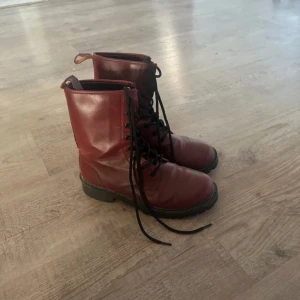 Röda boots från Vox Shoes, storlek 39 - Snygga röda boots från Vox Shoes i storlek 39. Skorna har snörning framtill, rund tå och platt sula. Tillverkade i skinn med svarta detaljer och grov yttersula som ger en cool look. Perfekta för dig som gillar att sticka ut med färg på fötterna.