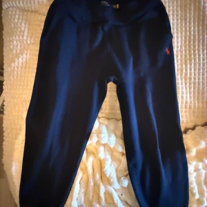 Mörkblå mjukisbyxor Polo Ralph Lauren - Snygga mörkblå mjukisbyxor från Polo Ralph Lauren med klassisk röd logga på benet. Byxorna har elastisk midja och muddar vid bensluten för skön passform. Tillverkade i mjukt bomullsmaterial, perfekta för chill eller träning.