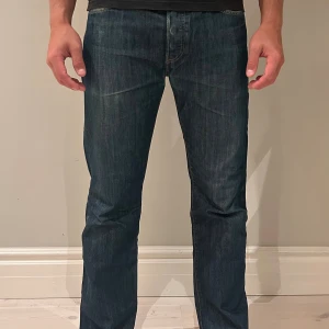 Levi's 501 mörkblå jeans W33 L32 - Klassiska Levi's 501 jeans i mörkblå tvätt med raka ben och normal passform. Jeansen har fem fickor, knappgylf och är tillverkade i slitstarkt bomullsdenim. Perfekta för dig som gillar tidlös stil och vill ha ett par riktigt schyssta jeans.