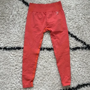 Gymshark Träningstights <3 - Snygga leggings från Gymshark med hög midja och diskret mönster. Stretchigt material som sitter tight och bekvämt, perfekt för träning. Gymshark-logga i vitt på höften och benet. Superskön passform och cool färg, korall, orange/röd. Storlekslappen är avklippt men de är storlek M <3