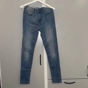 Lee Scarlett High ljusblå jeans W29 L31 - Snygga ljusblå jeans från Lee, modell Scarlett High med hög midja och klassisk femficksdesign. Jeansen har raka ben och Lee-logga på bakfickan samt läderpatch i midjan. Perfekt passform och mjukt denimtyg. En sån skärpflärp har gått upp, lätt att fixa dock för den som har tiden!