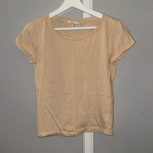 Beige kortärmad topp från H&M XS - En enkel och stilren beige topp från H&M i storlek XS. Modellen har rund halsringning och korta ärmar. Tillverkad i mjuk bomull som känns skön mot huden. Perfekt att matcha med jeans eller kjol för en clean look.