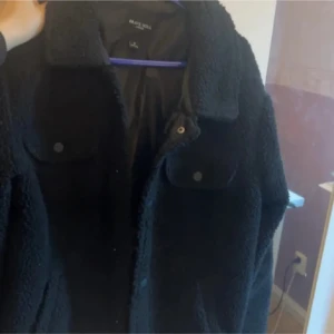 Svart teddyjacka Brave Soul S - Svart teddyjacka från Brave Soul i storlek S. Jackan har krage, två bröstfickor med knappar och en mjuk, fluffig yta. Perfekt för dig som gillar en chill och cozy stil under höst och vinter. Enkel att matcha med jeans eller hoodies.