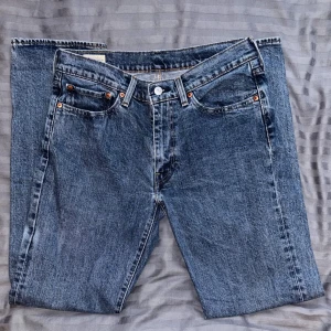 Levi's 514 blå jeans W32 L32 - Säljer ett par klassiska Levi's 514 jeans i blå tvätt med raka ben och fem fickor. Jeansen har orangea nitar, knappgylf och den ikoniska läderpatchen bak. Perfekt passform för dig som gillar en tidlös och avslappnad stil.