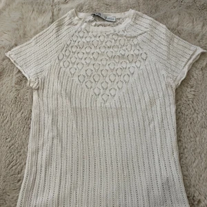 Vit topp från Zara - Säljer en vit blus från Zara i storlek S. Toppen har korta ärmar och ett snyggt hålmönster med både vertikala ränder och dekorativa former framtill. .