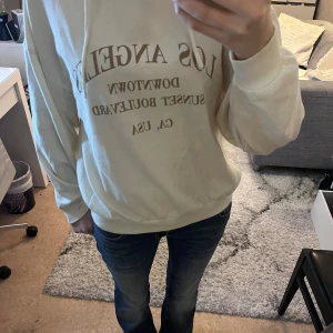 Beige hoodie med Los Angeles-tryck - Säljer en beige hoodie med tryck i brunt. Tröjan har huva med snörning och långa ärmar. Perfekt för en chill och avslappnad stil.