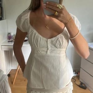 Vit blus med puffärm och knappar - Säljer en söt vit blus med diskreta ränder, puffärmar och v-ringad hals. Blusen har knappar framtill och är lätt utsvängd nedtill. Den är från brandy och knappt använd!!🩷🩷
