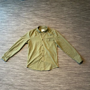 Olivgrön skjorta från Vailent Pure - Olivgrön skjorta från Vailent Pure i storlek M. Skjortan har klassisk krage, bröstficka och knappar hela vägen framtill. Tillverkad i mjuk bomull med långärmad passform och enkel, stilren design. Perfekt för dig som gillar minimalistisk stil.