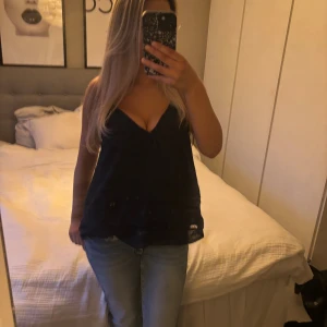 mörkblå linnetopp med v-ringning - Säljer en mörkblå linnetopp med djup v-ringning och tunna axelband. Toppen har en lös passform och är lätt och luftig, perfekt för varma dagar. Materialet känns mjukt mot huden och ger en avslappnad vibe. Passar dig som gillar enkel och stilren look.