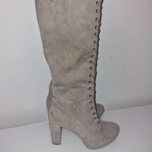 Grå höga mockastövlar med snörning - Snygga höga stövlar i ljusgrå mocka med grov klack. Stövlarna har snörning hela vägen upp och dragkedja på sidan. Använd vid 1 tillfälle, snygga både till jeans & kjol 🩶 Dyra vid inköp