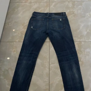 Mörkblå jeans från Dsquared2, strl 48 - Snygga mörkblå jeans från Dsquared2 i klassisk femficksmodell. Jeansen har slitna detaljer och en straight passform som ger en cool vibe. Materialet är robust jeans och färgen har snygga tvättade partier. Perfekt för dig som gillar streetstyle och vill ha ett statement-plagg.