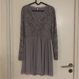 Ljuslila spetsklänning från NLY TREND - Superfin ljuslila kortklänning från NLY TREND med långärmade spetsdetaljer och v-ringad hals. Överdelen har blommigt spetsmönster och kjolen är lätt och flödande. Endast använd en gång.