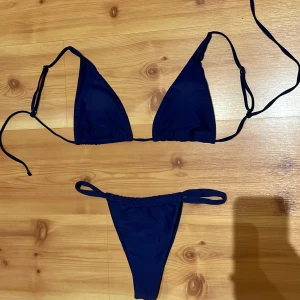 Mörkblå trekantsbikini med knyt - Snygg mörkblå bikini med klassisk trekantsmodell och knyt i sidorna både upptill och nedtill. Perfekt för stranden eller poolen, enkel att justera för bästa passform. Stilren och tidlös design som passar till allt. Använts 1 gång. 