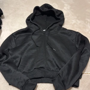 Svart hoodie med huva och snörning - En stilren svart hoodie med huva och snörning. Tröjan har långa ärmar, ribbade muddar och midja. Tillverkad i mjukt material som känns skönt mot huden. Perfekt för en avslappnad look.