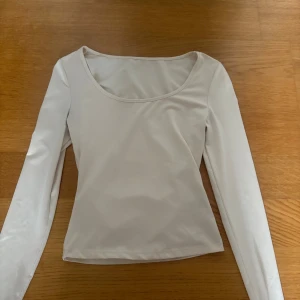 Vit långärmad topp med rund hals - Säljer en stilren vit långärmad topp med rundad halsringning. Toppen har en enkel och clean design, perfekt att matcha med jeans eller kjol. Materialet känns mjukt och stretchigt, vilket gör den bekväm att bära hela dagen.