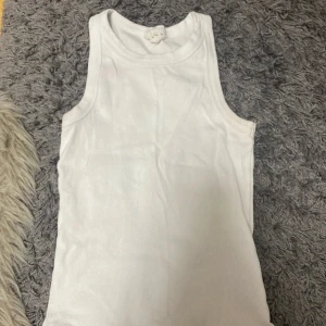 Vit ribbad linnetopp från Gina Tricot - Säljer en klassisk vit ribbad linnetopp från Gina Tricot, kollektionen Basically Basics. Toppen är ärmlös med rund halsringning och har en tight passform. Perfekt att styla med jeans eller kjol för en clean och enkel look.