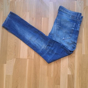 Blå Diesel jeans med slitningar - Säljer ett par blå jeans från Diesel med snygga slitningar och lätt tvättad look. Jeansen har klassisk femficksdesign, smal passform och detaljer som ger en cool, avslappnad vibe. Perfekta för dig som gillar streetstyle och vill ha ett par jeans som sticker ut. Nypris:1299