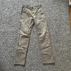 Beiga chinos från Lindex stl 164 - Snygga beiga chinos från Lindex i storlek 164. Klassisk rak passform med fickor fram och bak, bälteshällor och knappstängning. Perfekta till en avslappnad stil och tillverkade i mjuk bomull för skön känsla hela dagen.