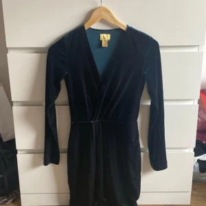 Mörkblå sammetklänning omlott - Supersnygg mörkblå klänning i sammet från H&M med omlottmodell och långa ärmar. Djup v-ringning och markerad midja ger en elegant siluett. Perfekt för dig som vill sticka ut med en lyxig känsla.