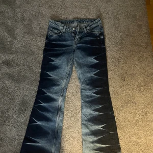 Blå bootcut jeans med coolt mönster - Säljer ett par blå jeans med bootcut-modell och unikt, nästan zigzag-liknande mönster längs benen. Klassisk femficksdesign och låg midja. Älskar de, men säljer då de är lite små för mig🥰 