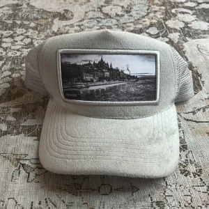 Grå keps från Resore med fototryck - Snygg grå keps från Resore med mjuk mockaliknande front och mesh baktill. Framtill sitter ett svartvitt fototryck av en stadsmiljö. Justerbar snapback och broderad logga på insidan. Perfekt accessoar för en cool och avslappnad stil.