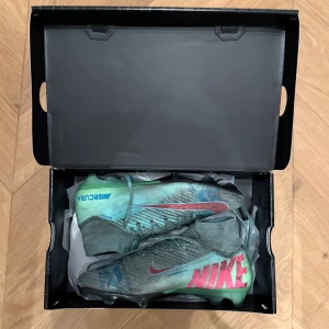 Nike Mercurial fotbollsskor - Säljer dessa NIKE AIR ZOOM MERCURIAL SUPERFLY 10 ELITE FG COSMIC SPEED 2 - HYPER TURKOS/SVART LIMITED EDITION. Riktigt feta fotbollsskor som är limiterade och slutsålda. Relativt bra skick, inget som är trasigt. Men det finns tydliga täcken på användning av skorna på konstgräs. De är i storlek 41. Box och påse följer med. Pris kan diskuteras