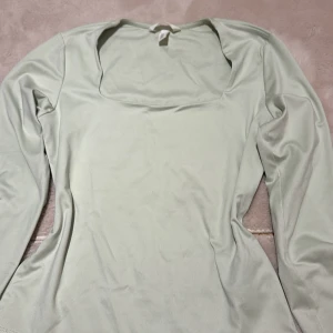 Ljusgrön långärmad topp H&M - Säljer en ljusgrön långärmad topp från H&M med fyrkantig ringning. Toppen är i mjukt och stretchigt material, perfekt för en clean och stilren look. Passformen är normal och den är enkel att matcha med både jeans och kjol.