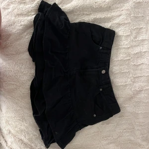 Svart jeans volangkjol från Zara - Supersnygg svart kortkjol från Zara med volangkant och klassisk jeanslook. Kjolen har fickor fram och bälteshällor i midjan. Perfekt för dig som gillar en trendig och stilren vibe.