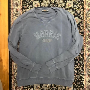 Blå sweatshirt från Morris, storlek L - Säljer en blå sweatshirt från Morris med broderad logga och texten 'Morris på bröstet. Tröjan har rund halsringning, ribbade muddar och är tillverkad i mjuk bomull. Perfekt för en avslappnad och stilren look.