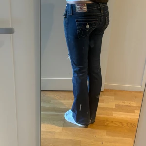 True religion bootcut jeans - Snygga Lågmidjade true religion jeans i mörkblå tvätt med bootcut. Slitning och hål på ena knäet. Dom är uppsprättade och lite slitna längst ner som man ser på sista bilden. Jag är 167cm.💓skriv för fler bilder eller frågor! 
