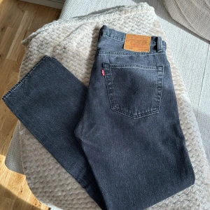 Levi's 501 gråa jeans - Snygga mörkgråa Levi's 501 jeans med klassisk rak passform och femficksdesign. Jeansen har en mörk tvätt och är tillverkade i slitstarkt bomullsjeans. Perfekta för dig som gillar en tidlös och avslappnad stil. Storlek 31/30