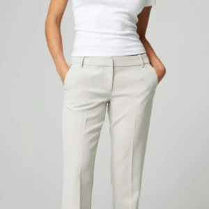 Beiga kostymbyxor med raka ben - Snygga lågmidjade beiga kostymbyxor med raka ben och pressveck från bikbok. Byxorna har hällor för bälte, diskreta fickor fram och bak samt en klassisk midja. Perfekta för en clean och stilren look.