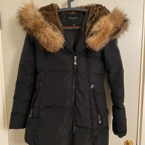 Svart dunjacka med päls från Hollies - Använts en vinter, tvättbjörn pälsen runt luvan är avtagbar men pälsen i luvan (inte äkta) går inte att ta av. Nypris 5000 kr.