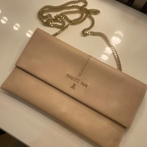 Patrizia Pepe väska i Begie - Väskan är i fint skick men har dn liten smink fäck innuti. Perfekt att använda som en fest väska. Måtten är ca 16x 28cm. Har tyvärr inget kvitto kvar.