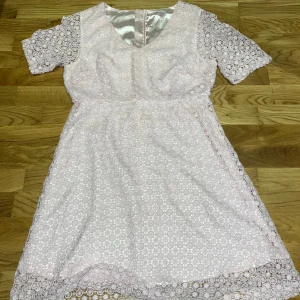 Ljusrosa spetsklänning med dragkedja - Superfin ljusrosa kortklänning med blommig spets och silkeslen insida. Klänningen har korta ärmar, v-ringning och en snygg guldig dragkedja bak. Perfekt för dig som gillar romantiska detaljer och en feminin look. Man ser inte på bilderna hur rosa den egentligen är men den är i en extremt rosa fin färg. Storlek 40. Säljs för endast 199