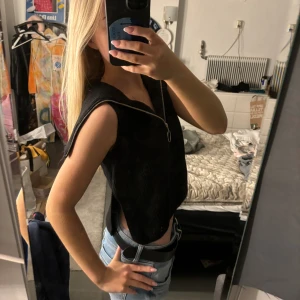 Svart stickad topp från Vero Moda - Svart stickad topp från Vero Moda i croppad modell. Västen har en markerad v-ringning med en dragkedja framtill och är ärmlös med breda axelpartier. 