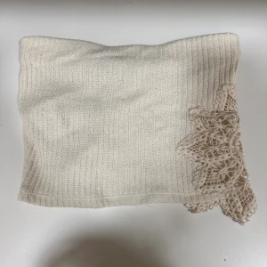 Beige stickad tubtop med spets från Zara - Supersöt beige stickad tubtop från Zara med ribbad struktur och dekorativ spetsdetalj i ena hörnet. Perfekt för att ge din outfit en extra touch av stil. Helt oanvänd med prislappen på och k storlek S!