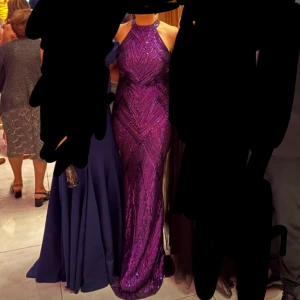 Lila glittrig långklänning med halterneck - Säljer en superfin lila långklänning med glittriga paljetter och halterneck. Perfekt för dig som vill sticka ut på bal eller fest! Endast använd i några timmar och är som ny!