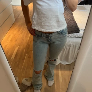 Ljusblå bootcut jeans med slitningar - Fina jeans ifrån Nelly med hål på båda knäna. Rosa design på fickorna. Booutcut och lågmidjade! Använda fåtalet gånger så i mycket fint skick! Något slitna nedtill då de är för långa för mig. Köpta för 700kr! Innerbenslängden 80cm, midjemåttet runt om 60 cm.