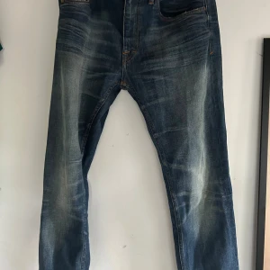 Blå Iggy jeans 32/32  - Snygga blå jeans från tiger of sweden i modellen Iggy. storlek 32/32. Jeansen har ljusare partier framtill och baktill för en avslappnad vibe. Klassisk femficksmodell med raka ben och orangea sömmar. Perfekta för dig som gillar en casual streetstil.