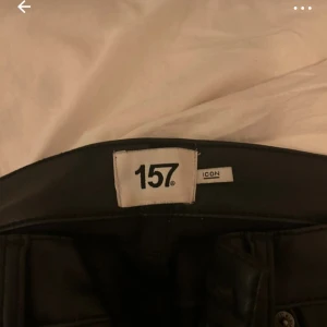 Svarta skinbyxor  - Säljer ett par svarta byxor från 157 i skinnimitation. De har klassisk femficksdesign, raka ben och normal passform. Snygga detaljer med dragkedja och markerade sömmar. Perfekta för dig som vill ha en edgy look.