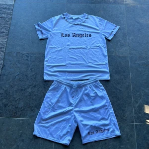 Vitt Mjukis/tränings set - Vitt mjukis/tränings set med ett Los Angels tryck på både T-shirten och shortsen. Aldrig använt det och helt nytt skick. Snyggt set som passar i vardagen. Ordinarie pris på det var 65 kr. 
