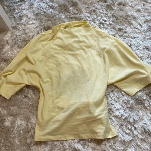 Gul omlottopp med knyt  - Säljer en ljusgul omlottopp  i mjuk bomull. Toppen har korta ärmar och en snygg knytning i ryggen som ger en unik look. Perfekt för dig som gillar en chill men ändå trendig stil. Passar till både jeans och kjol.