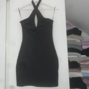 Svart kort klänning  - Supersnygg svart kort klänning från H&M Divided med korsad halterneck. Klänningen har en tight passform och en liten cut-out framtill som ger en trendig look. Perfekt för dig som gillar stilrena och moderna plagg.