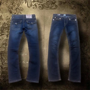 True Religion jeans Billy Super T - Använda endast ett fåtal gånger och köpta tidigare i år – i stort sett som nya. Modell: Billy Super T (passformen är mer åt det smalare hållet, inte särskilt bootcut eller flared).  || Midja: 38 cm 	Innerbenlängd: 79–80 cm 	     Ytterbenlängd: 103 cm 	       Lår: 20 cm  || Som referens: tjejen på bilderna är 172–173 cm lång och brukar ha XS/XXS. Storlek: W27   ||    Kan mötas upp i Stockholm.