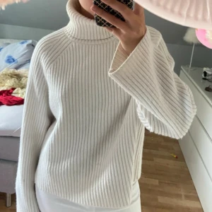 Vit ribbad polotröja i stickat material - Säljer en vit ribbstickad polotröja med hög krage och långa ärmar. Tröjan har en loose fit och är supermjuk och skön, perfekt för kyliga dagar. Enkel att styla med både jeans och kjol för en clean look.