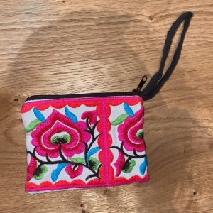 Broderad korthållare med blommor - Färgglad korthållare med broderade blommor i rosa, rött, grönt och blått. Korthållaren har dragkedja och en praktisk handledsrem. Köpte i Thailand❤️