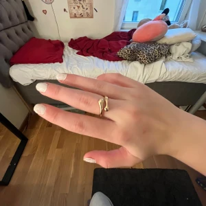 Guldig chunky ring med unik form - Säljer en snygg guldig ring med chunky design och cool, böjd form. Ringen har en öppen detalj framtill som ger den en modern och trendig look. Perfekt accessoar för att lyfta din outfit och sticka ut lite extra.