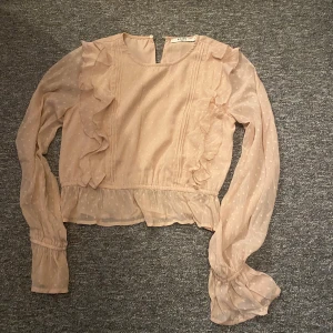 Ljusrosa blus med volang från NA-KD - Supersöt ljusrosa blus från NA-KD med volangdetaljer längs sidorna och ärmarna. Blusen är använd en gång och är i storlek S